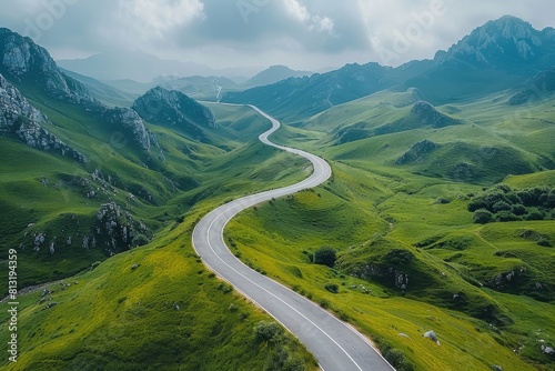 Birds-eye view of a winding road through lush green rolling hills under a cloudy sky