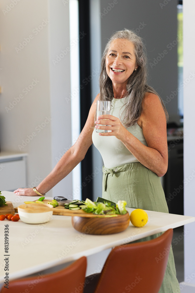 At home, mature Caucasian woman preparing food, holding a glass of water At home, mature Caucasian woman preparing food, holding a glass of water