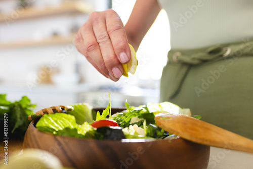 At home, mature caucasian woman squeezing lemon juice over salad photo