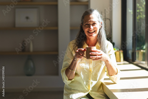 At home, mature caucasian woman wearing yellow shirt, enjoying coffee, copy space photo