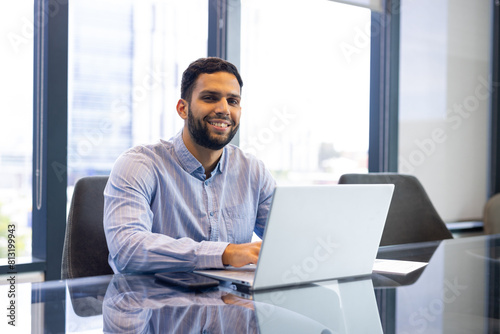 A biracial young professional man, sitting at office desk, typing on laptop photo