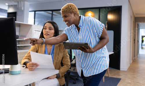 At office, diverse team member pointing at screen, holding business papers photo