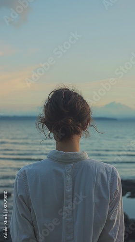 Woman white shirt stands shoreline dusk looking peaceful ocean distant clouds