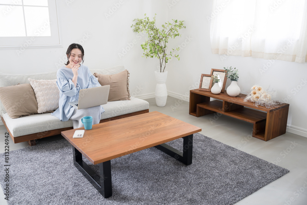 Woman using a computer sitting in the living room Image of a woman working remotely or at home Looking at a computer, searching and thinking Full body Woman using a computer sitting in the living room Image of a woman working remotely or at home Looking at a computer, searching and thinking Full body