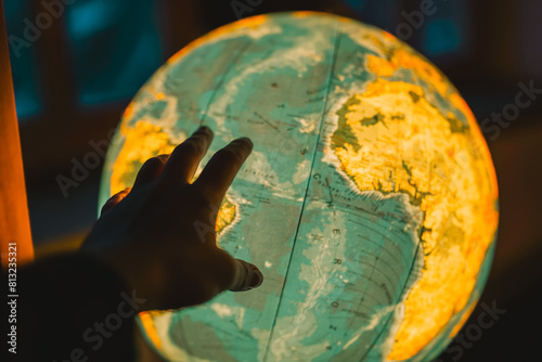 Interactive Geography  Searching for a Country.Exploring the World  A hand reaches out to a glowing globe in a dark room. Educational Journey  Luminous Globe and Seeks Out Names of Countries.