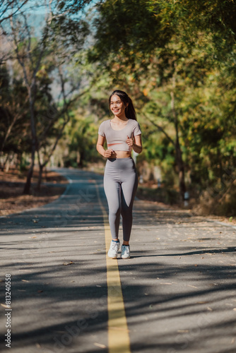 Cheerful young woman in fitted athletic wear enjoys a solitary run on a sun-dappled path through the woods. © Mongta Studio