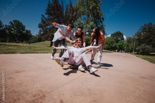 A group of young friends enjoying a sunny day in the park, playfully riding and pushing a skateboard together, showing joviality and companionship. photo