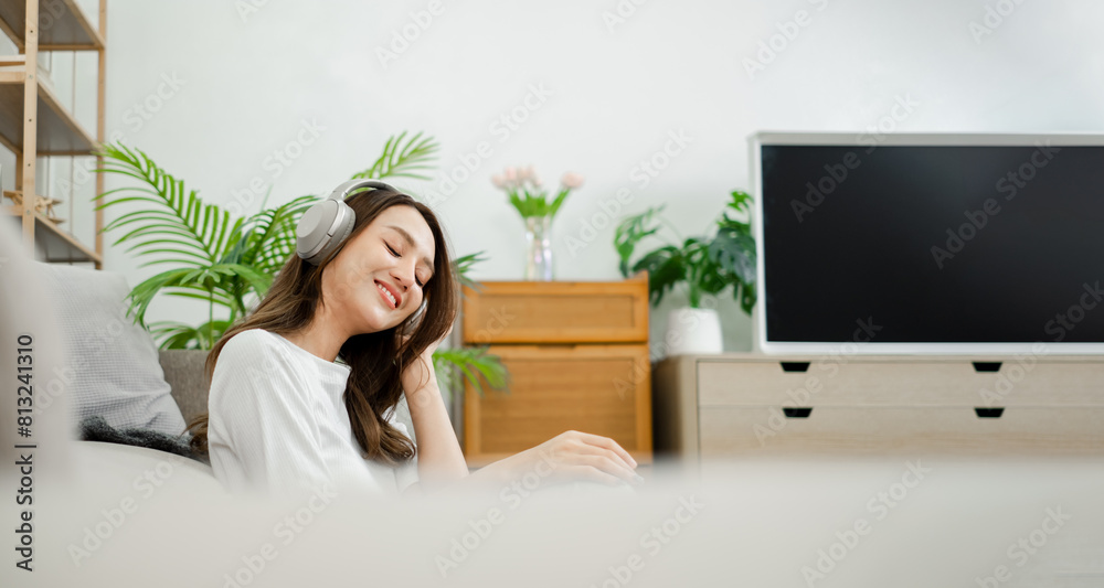 Contented woman closes her eyes, enjoying music through headphones, feeling relaxed in the comfort of her home decorated with plants. Contented woman closes her eyes, enjoying music through headphones, feeling relaxed in the comfort of her home decorated with plants.