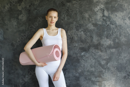 sporty woman in white sportswear with pink exercise roll mat in relaxed pose on stone background