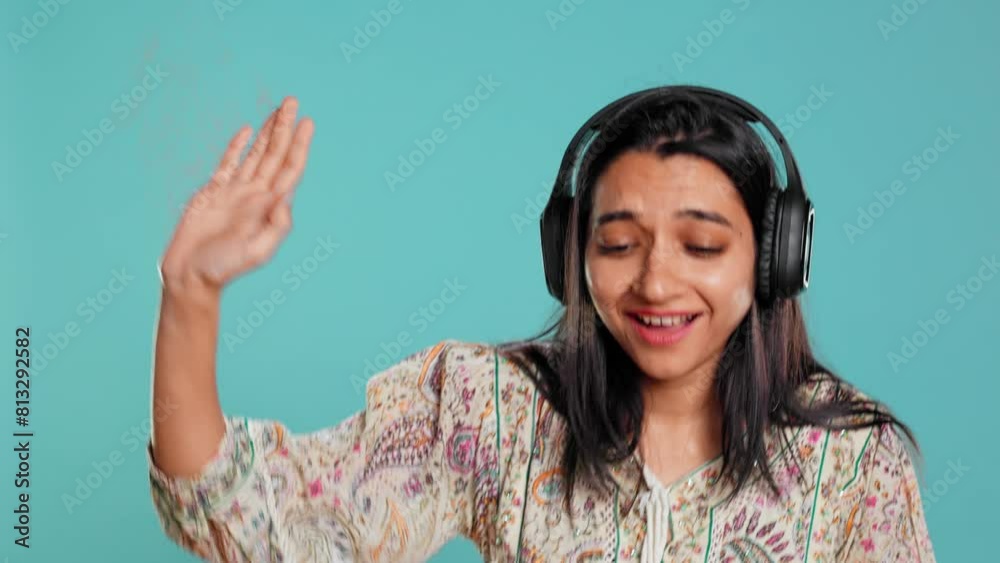 Indian woman playing music, having fun moving on rhythm, pretending to use turntables. Upbeat DJ wearing headphones, producing beats, isolated over studio background, camera B Indian woman playing music, having fun moving on rhythm, pretending to use turntables. Upbeat DJ wearing headphones, producing beats, isolated over studio background, camera B