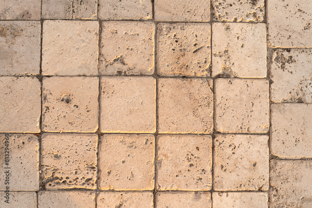 Naklejka premium The detail of worn stone paving blocks, showcasing their texture and the subtle color variations due to weathering. The natural light enhances the stones sandy tones