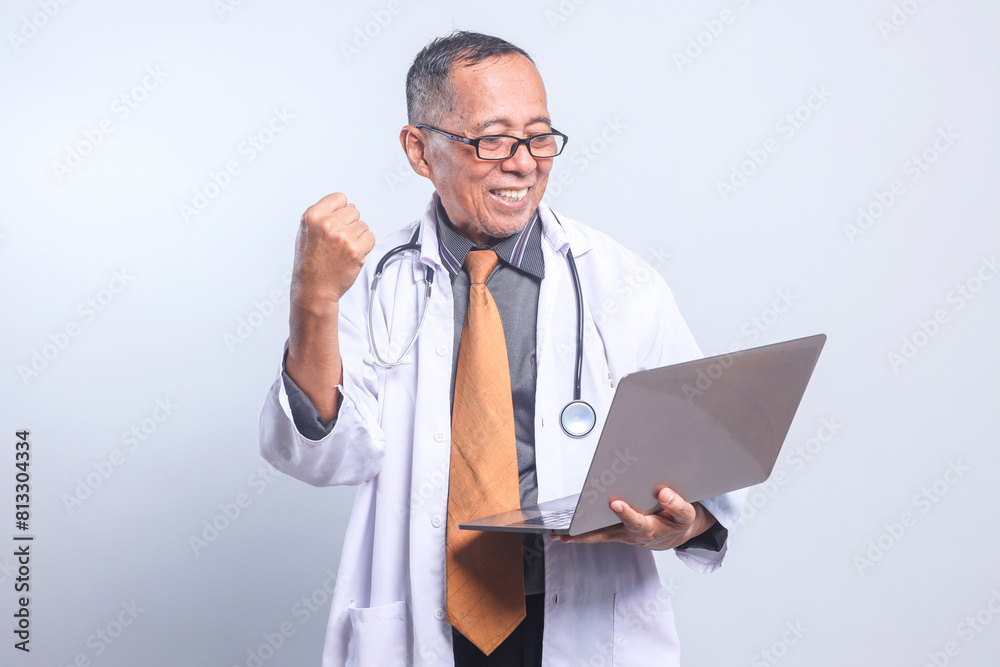 Cheerful Senior Doctor Male Looking At Laptop Clenching Fist Showing Success, Winning Gesture Isolated On White Background Cheerful Senior Doctor Male Looking At Laptop Clenching Fist Showing Success, Winning Gesture Isolated On White Background