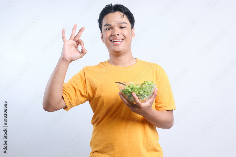 Cheerful Asian Guy Recommend a Healthy Food And Showing Ok Sign While Holding Vegetable Salad Bowl Isolated On White Background Cheerful Asian Guy Recommend a Healthy Food And Showing Ok Sign While Holding Vegetable Salad Bowl Isolated On White Background