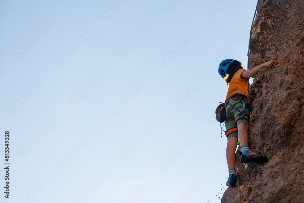 A determined and strong boy climber climbs a steep mountain wall. Extreme sports and rock climbing. A determined and strong boy climber climbs a steep mountain wall. Extreme sports and rock climbing.