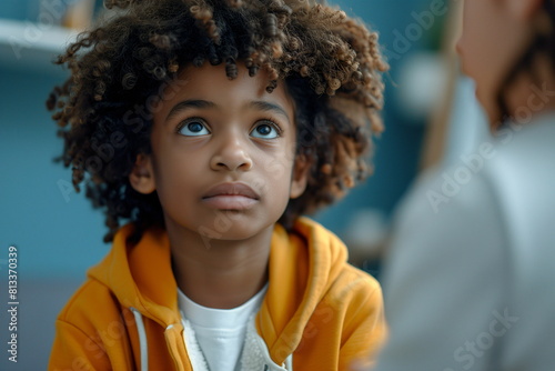 A boy with curly hair in a yellow hoodie looking up, appearing attentive and focused. Concept: ADHD.
