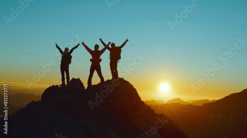 Three people are standing on a mountain peak, with the sun setting behind them