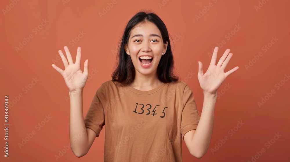 Excited young Asian woman with her hands up on a brown background. Excited young Asian woman with her hands up on a brown background.