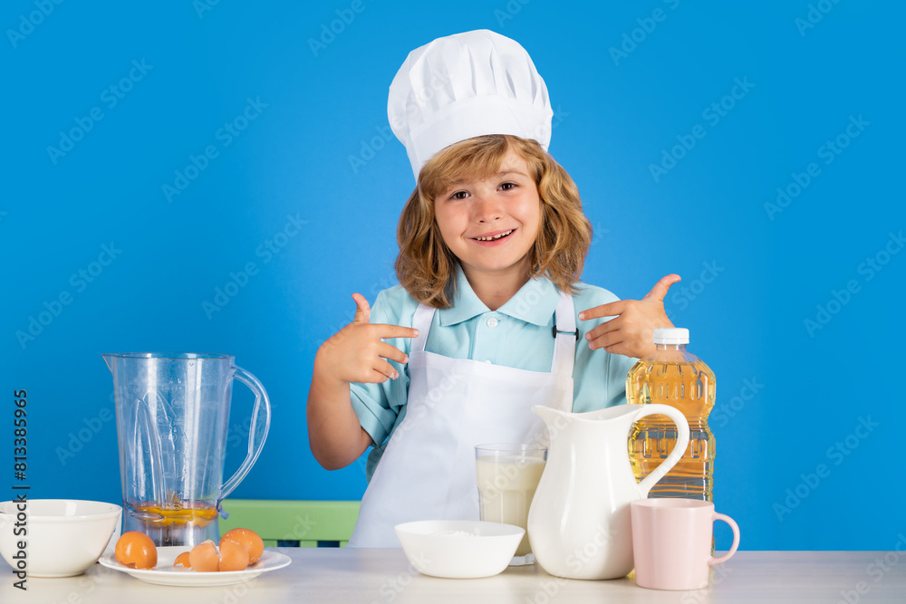 Child wearing cooker uniform and chef hat preparing vegetables on kitchen, studio portrait. Cooking, culinary and kids food concept.