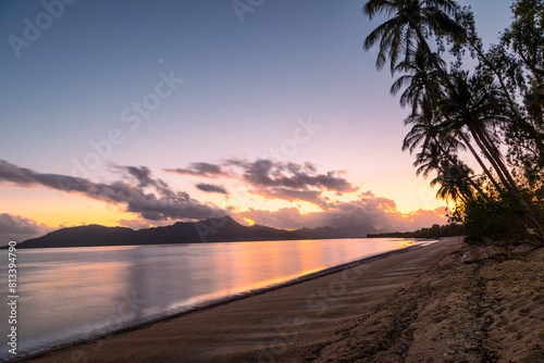 The sun rises over Hinchinbrook Island, part of the Great Barrier Reef National Park in this long exposure landscape photo with interesting colors, reflections, palms and a tropical beach in Australia photo