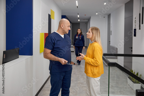 Doctor and female patient discussing something while standing in clinic corridor