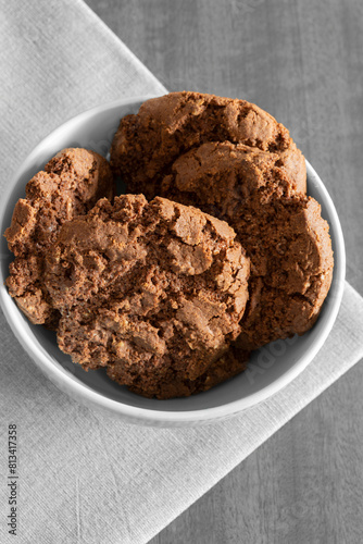 Chocolate flavoured cookies, with chocolate chips, in a green bowl on a tablecloth with a wooden background.
