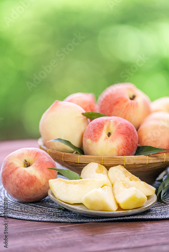 Fresh Sweet Peach on green bokeh background, Pink Peach fruit with leaf on wooden table. 