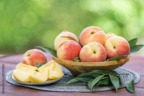 Fresh Sweet Peach on green bokeh background, Pink Peach fruit with leaf on wooden table. 