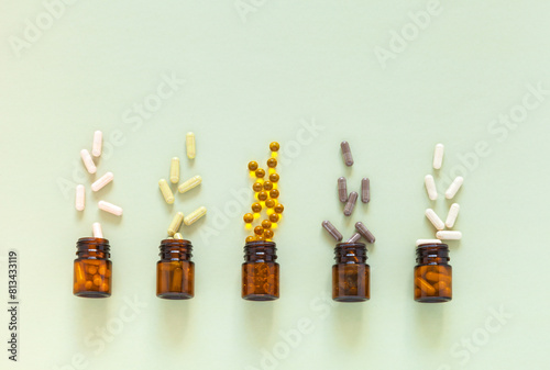 Top view of bottles with capsules of food bio additives on light green background. Five types of natural dietary supplements with herbals, vitamins and omegas. Flat lay, close-up, copy space