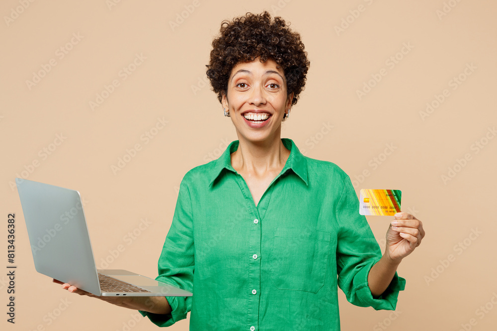Young IT woman of African American ethnicity in green shirt casual clothes use laptop pc computer hold credit bank card shopping online order delivery booking tour isolated on plain beige background Young IT woman of African American ethnicity in green shirt casual clothes use laptop pc computer hold credit bank card shopping online order delivery booking tour isolated on plain beige background