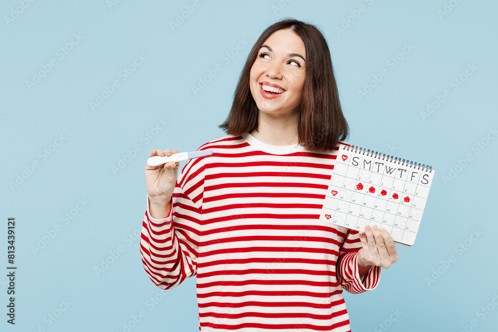 Young fun woman wear red casual clothes hold pregnancy test female periods pms calendar checking menstruation days look aside on area isolated on plain blue background. Medical gynecological concept. Young fun woman wear red casual clothes hold pregnancy test female periods pms calendar checking menstruation days look aside on area isolated on plain blue background. Medical gynecological concept.