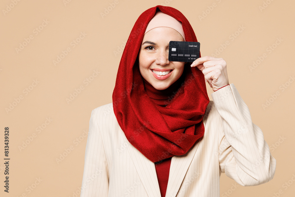 Young Arabian Asian Muslim woman wear red abaya hijab suit clothes hold cover eye with mock up of credit bank card isolated on plain beige background studio UAE middle eastern Islam religious concept Young Arabian Asian Muslim woman wear red abaya hijab suit clothes hold cover eye with mock up of credit bank card isolated on plain beige background studio UAE middle eastern Islam religious concept