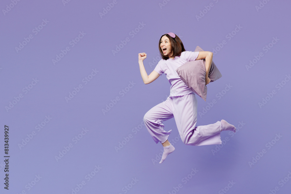 Fototapeta premium Full body side view young calm woman wear pyjamas jam sleep eye mask rest relax at home jump high run fast hold pillow isolated on plain pastel purple background studio. Good mood night nap concept.
