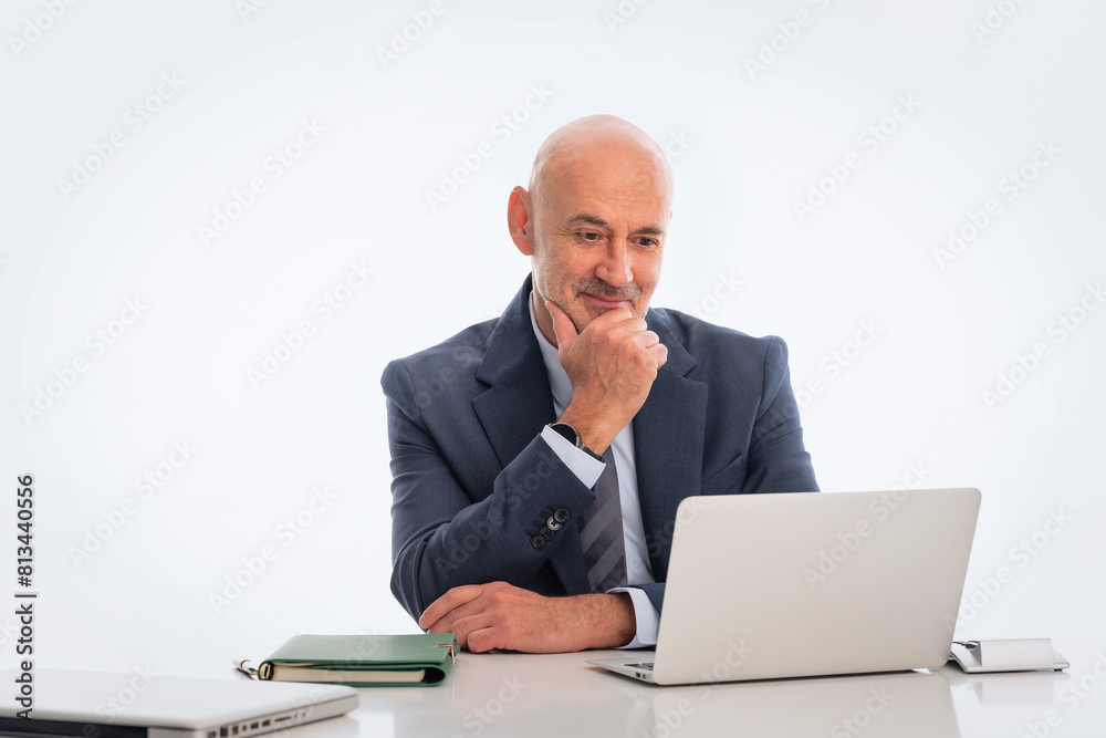 Mid aged businessman sitting at desk and using notebook for work against isolated background Mid aged businessman sitting at desk and using notebook for work against isolated background