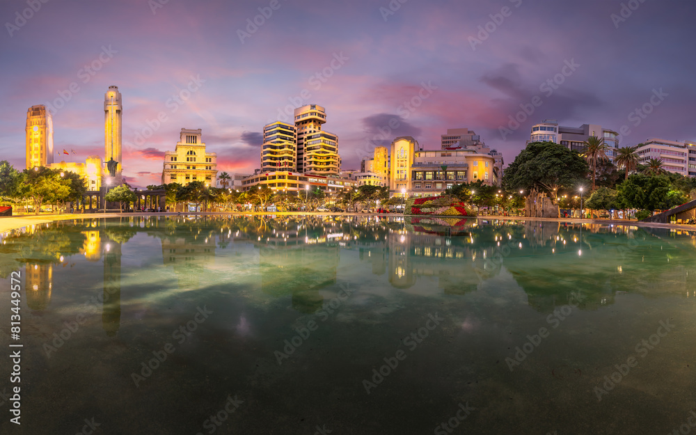 Twilight descends on Plaza de Espana, Santa Cruz de Tenerife, with stunning reflections and city lights creating a captivating urban scene.
