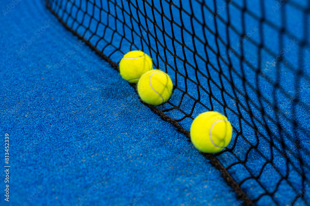  balls near the net of a blue padel tennis court