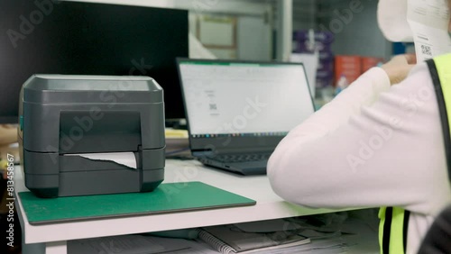 Woman uses a laptop or notebook to print bar code stickers on a bar code printer. Selective focus at sticker barcode.