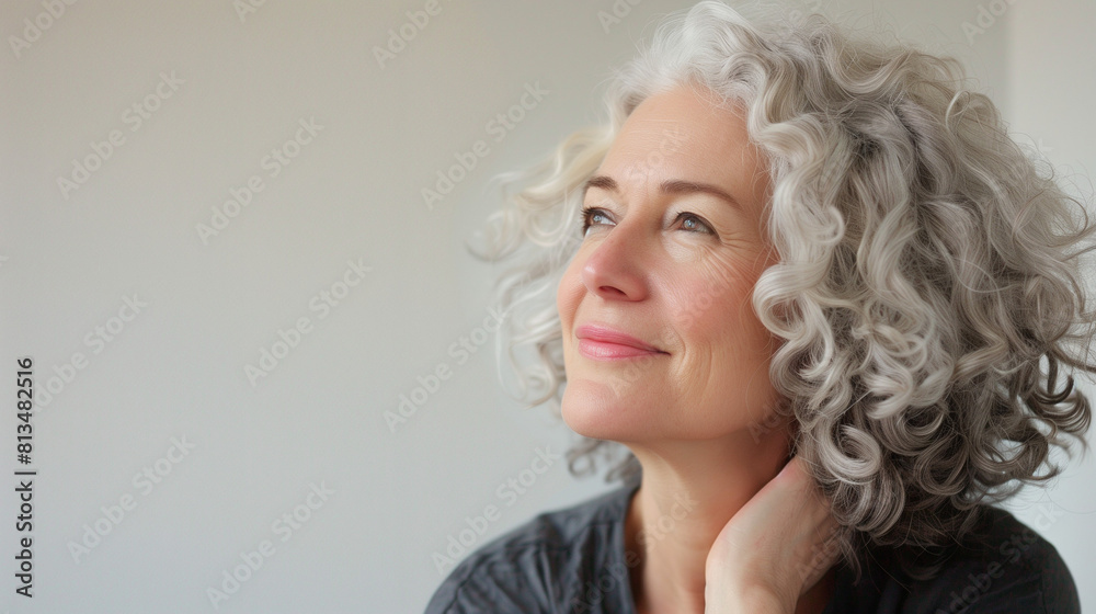 Middle-aged woman with curly silver and gray hair smiles in side view against white background.
