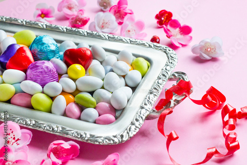 Colorful almond candy and chocolate silver tray designed with spring flowers on pink surface