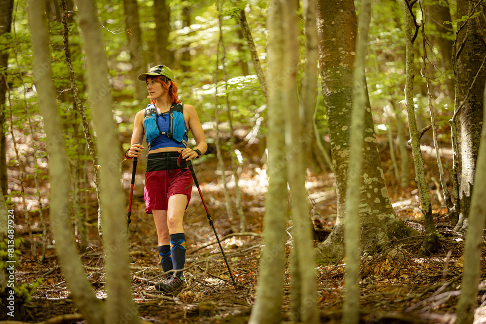 Obraz premium A woman is walking through a forest with a backpack on her back. She is wearing a blue shirt and red shorts