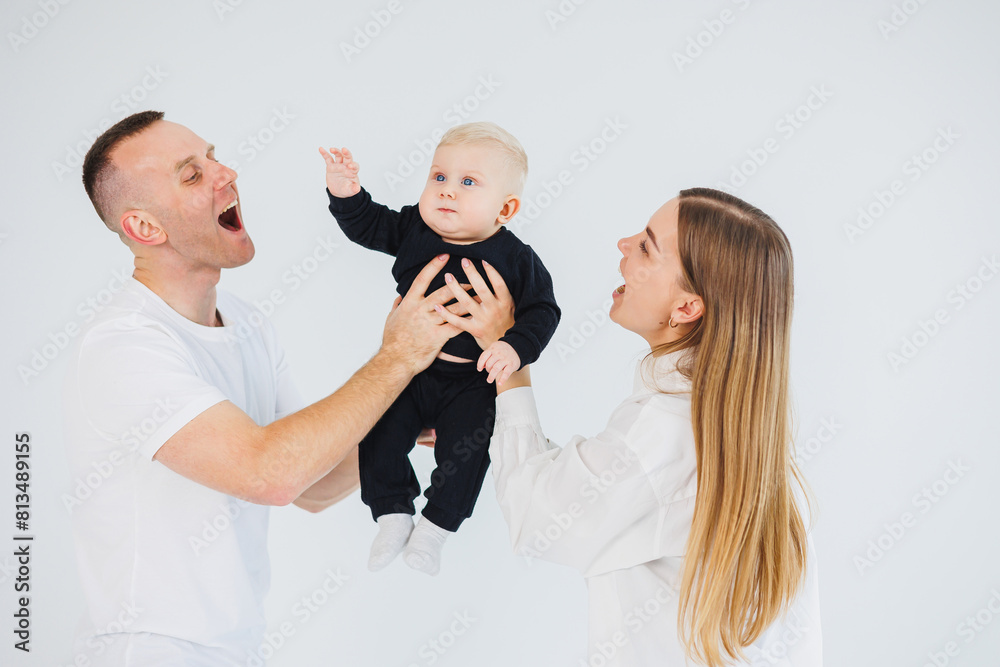 the father lifting 3 months new born baby boy on the air and kissing him, mother is watching smiling clapping cheering on the side the father lifting 3 months new born baby boy on the air and kissing him, mother is watching smiling clapping cheering on the side