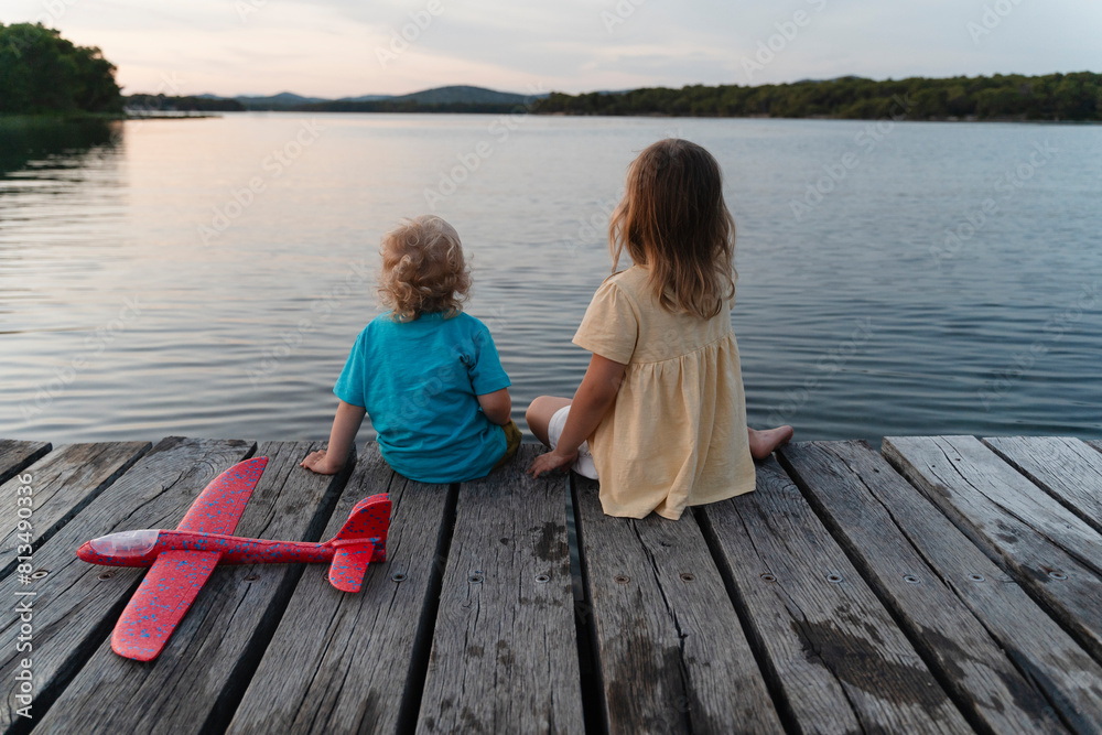 Brother and sister sitting on pier over lake Brother and sister sitting on pier over lake