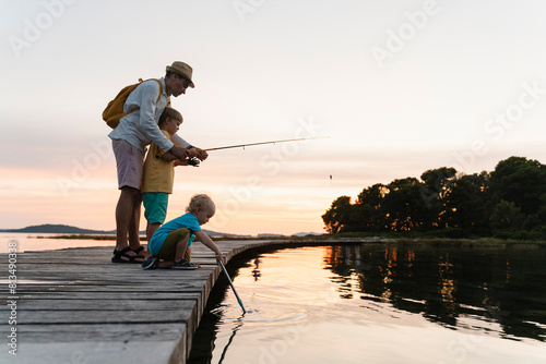 Father with sons fishing on pier over lake at sunrise photo