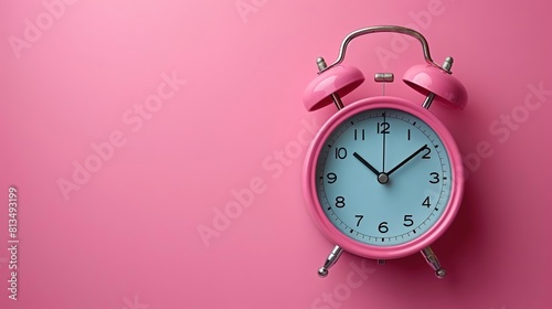 A pink alarm clock is sitting on a pink background. The alarm clock is set to 10:10.