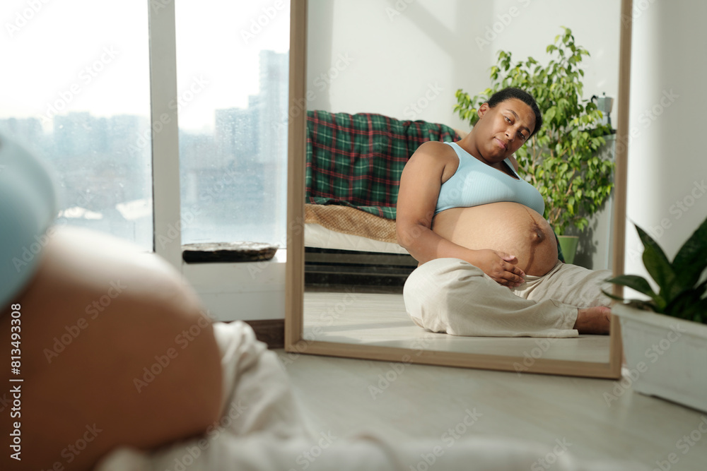 Plus size pregnant woman looking at mirror sitting on floor in room Plus size pregnant woman looking at mirror sitting on floor in room