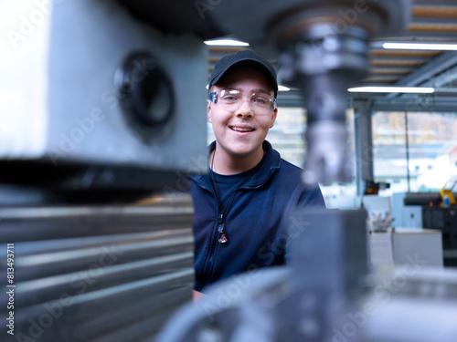 Smiling apprentice with safety goggles near machine at factory