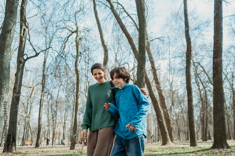 Happy mother and son walking together in front of trees at park Happy mother and son walking together in front of trees at park