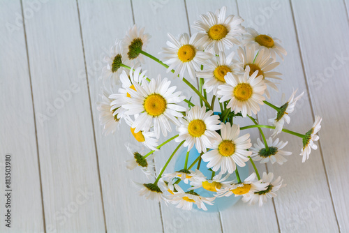 Bouquet of beautiful chamomile flowers in a vase on a white wooden background