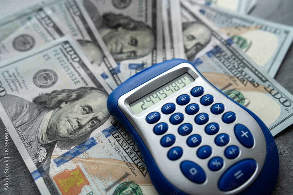 Many dollar bills and calculator on grey desk. Investment research data economy. Many dollar bills and calculator on grey desk. Investment research data economy.