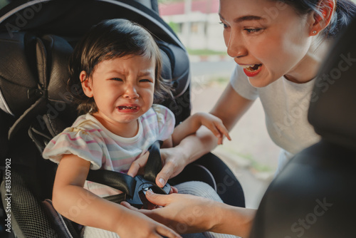 mother is fastening safety belt to crying toddler girl in car seat, safety baby chair travelling