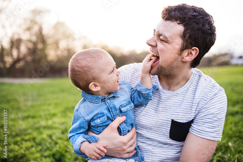 Father holding little toddler boy playing, having fun during warm spring day. Father's day concept.